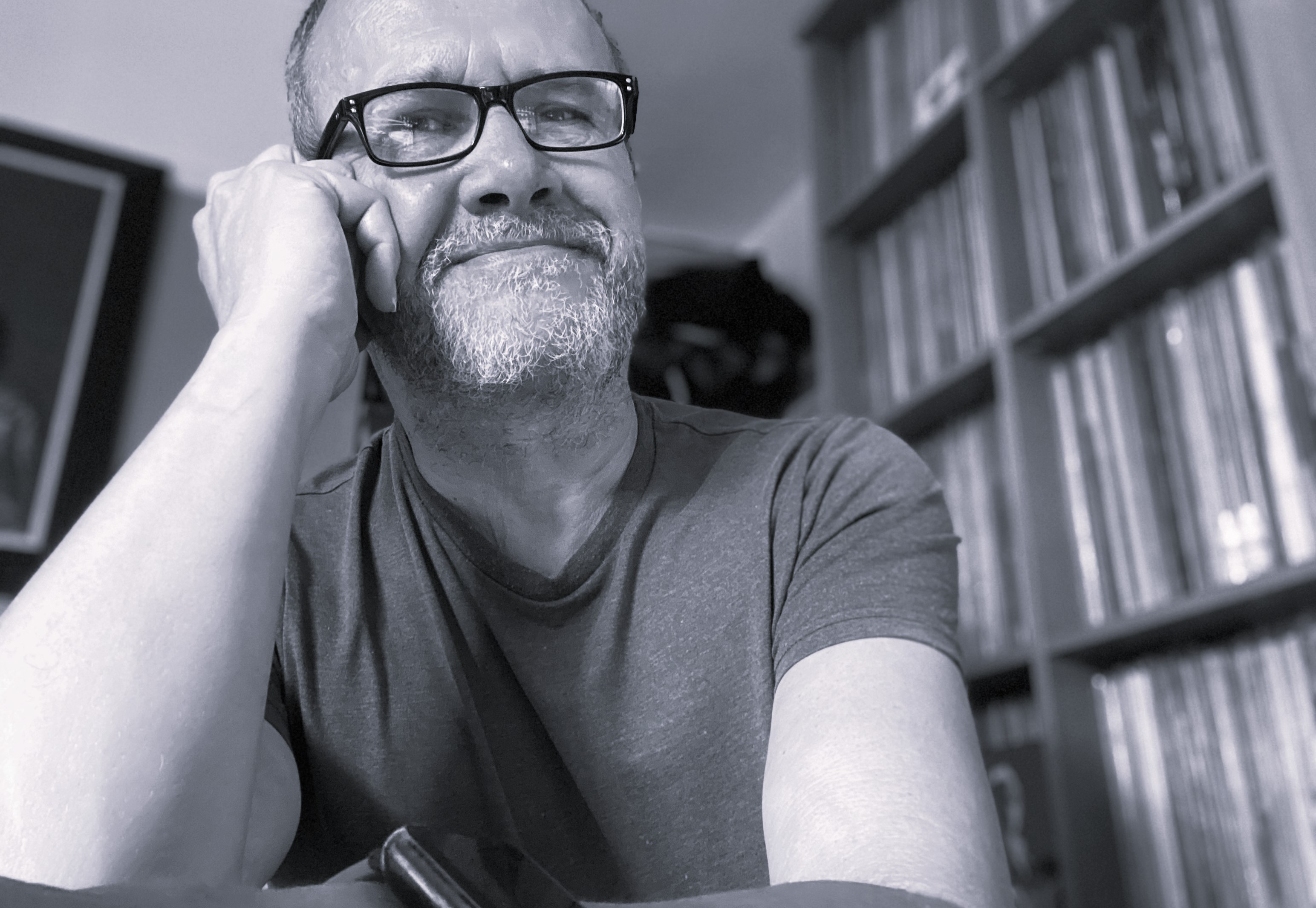 Peter Stoneman, seated, looking just past the camera, a wall of records behind him.